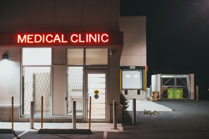 Entrada de uma clínica médica iluminada por letreiro neon durante a noite, sem pessoas visíveis
