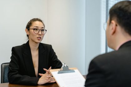 Candidato participa de uma entrevista de emprego em um escritório, enquanto uma profissional consulta anotações em uma prancheta.